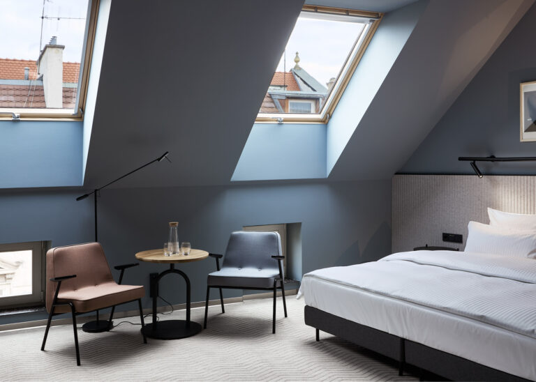 Jasny pokój Double King Room z dużym łóżkiem kontynentalnym, dwoma nowoczesnymi fotelami, drewnianym stolikiem kawowym oraz oknami dachowymi.