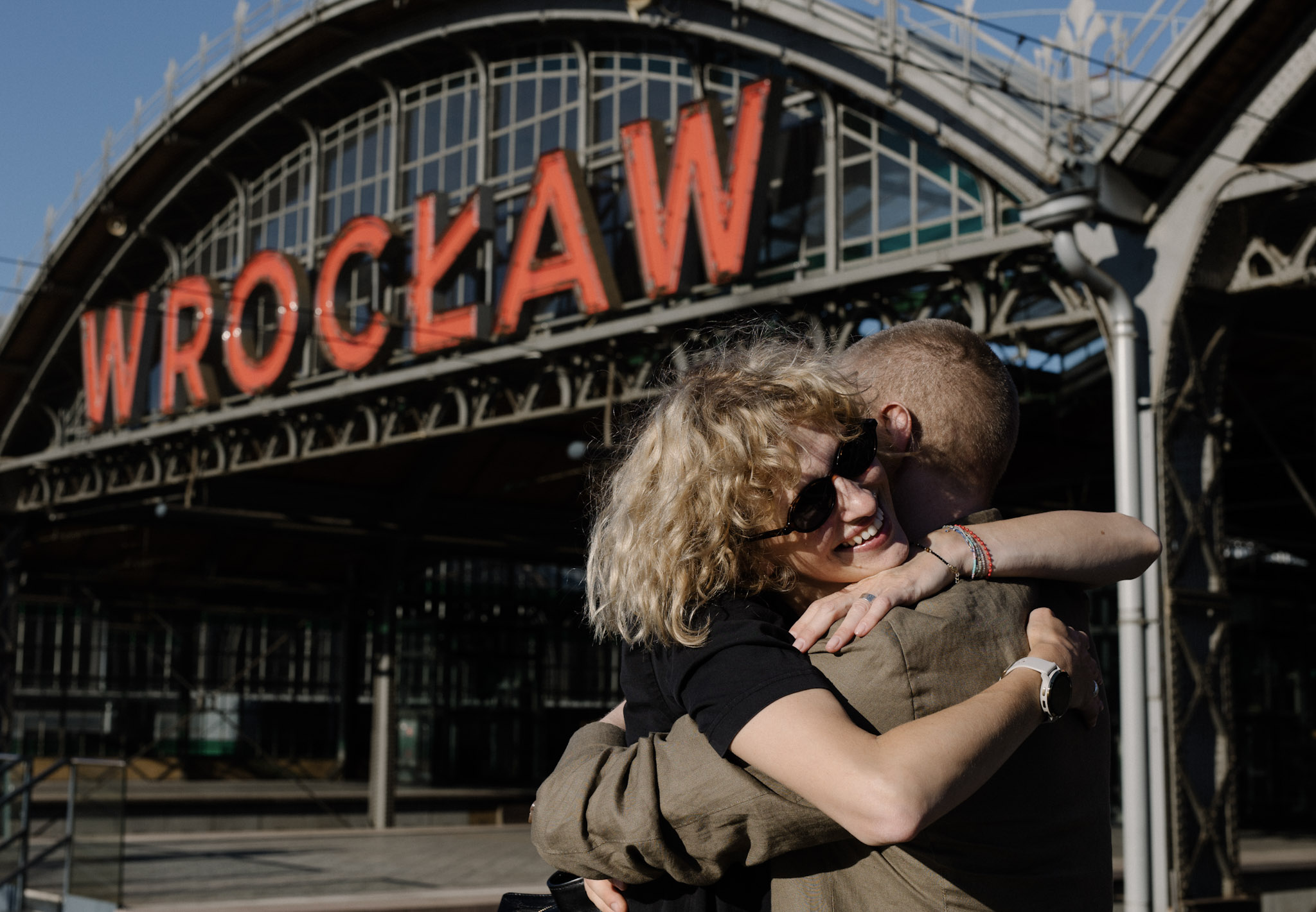 Para gości witająca się na zabytkowym Dworcu Głównym we Wrocławiu, na tle kultowego, historycznego napisu "Wrocław" nad peronami.
