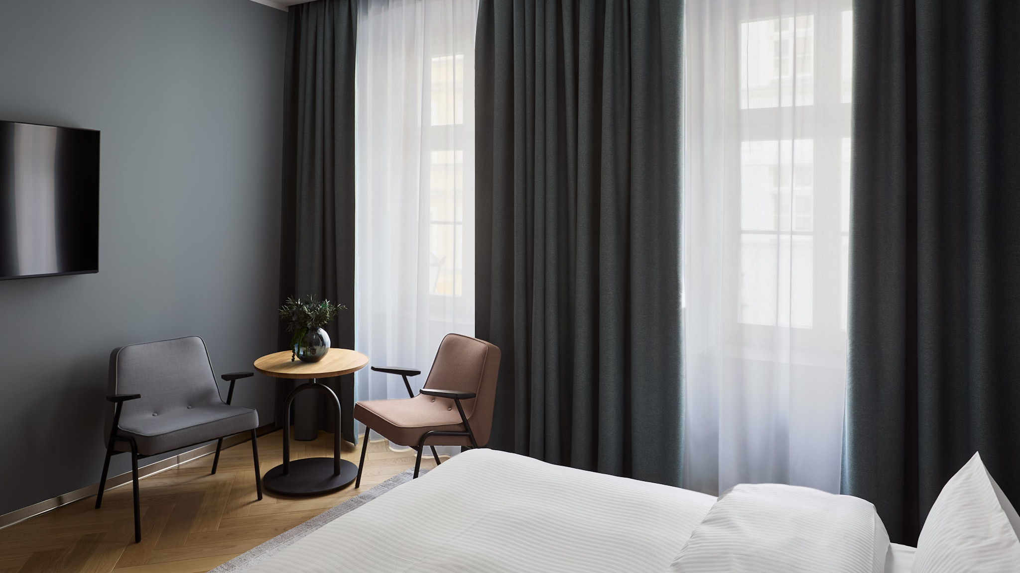 Strefa wypoczynkowa w apartamencie Executive Suite z dwoma nowoczesnymi fotelami, okrągłym stolikiem kawowym pod oknem oraz eleganckimi, ciemnymi zasłonami.