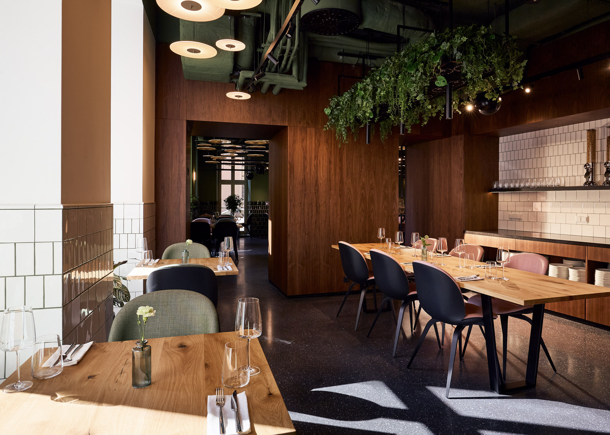 Nowoczesna restauracja Entre w stylu brasserie z drewnianymi stolikami, eleganckimi krzesłami, wiszącą zielenią oraz ciepłym wykończeniem w drewnie i płytkach.