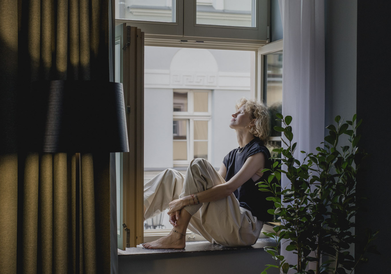 Urokliwy salon w apartamencie Executive Suite z widokiem na zabytkowe kamienice i rzekę przez duże okna. Wnętrze dopełnia klimatyczne oświetlenie i zielone rośliny.
