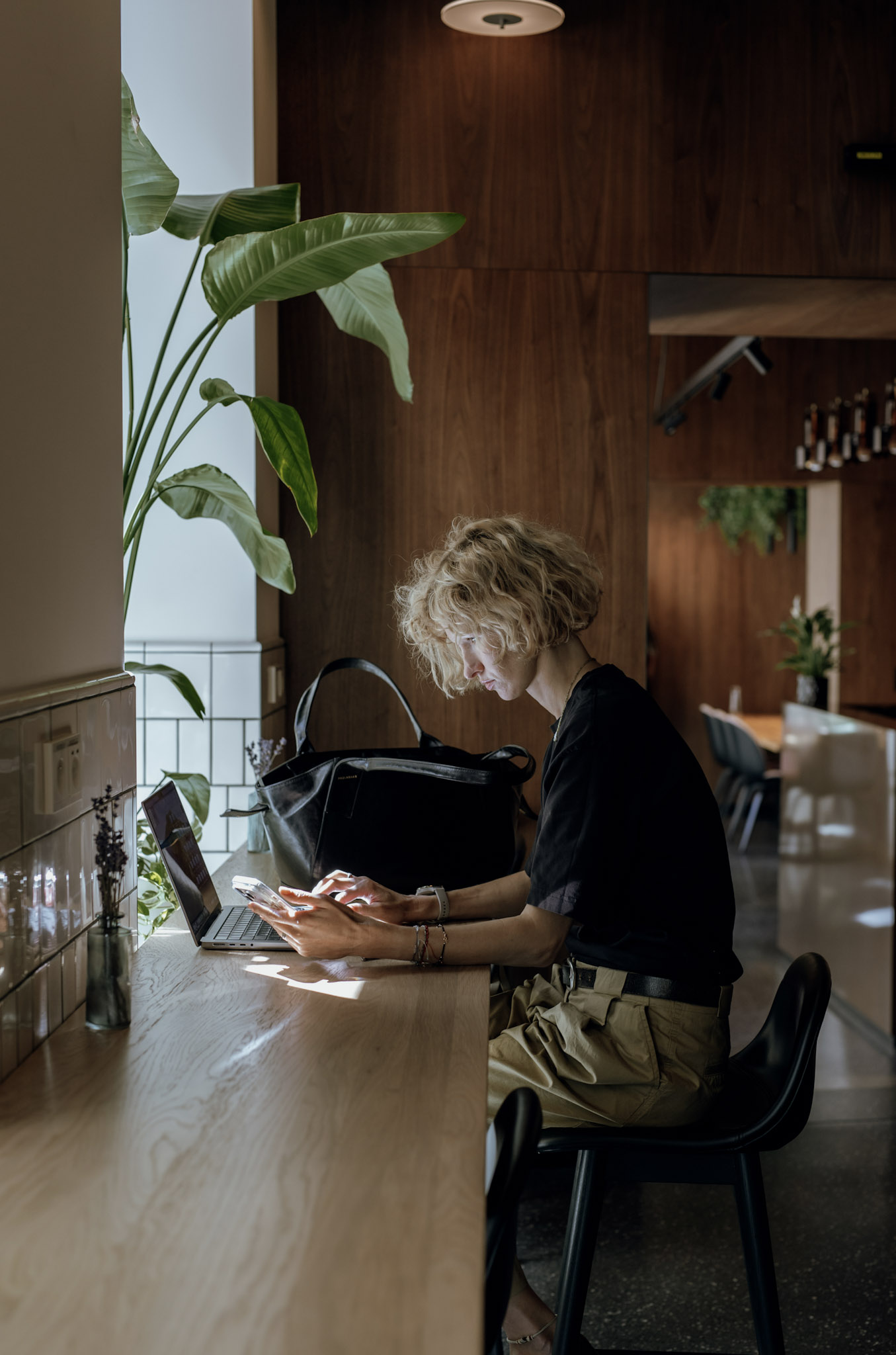 Kameralna strefa coworkingowa do cichej pracy z laptopem, wyposażona w podłużny drewniany blat, nowoczesne krzesła oraz duże rośliny doniczkowe w jasnym wnętrzu.